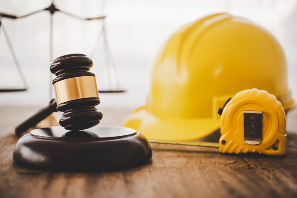 construction law with a gavel and a scale of justice and a hard hat and a tape measure on a desk